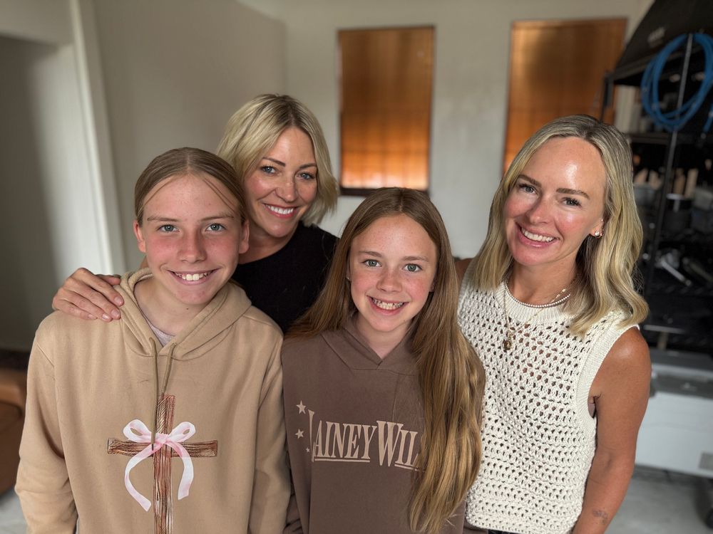 Four smiling women and girls posing together indoors, one wearing a Lainey Wilson hoodie.