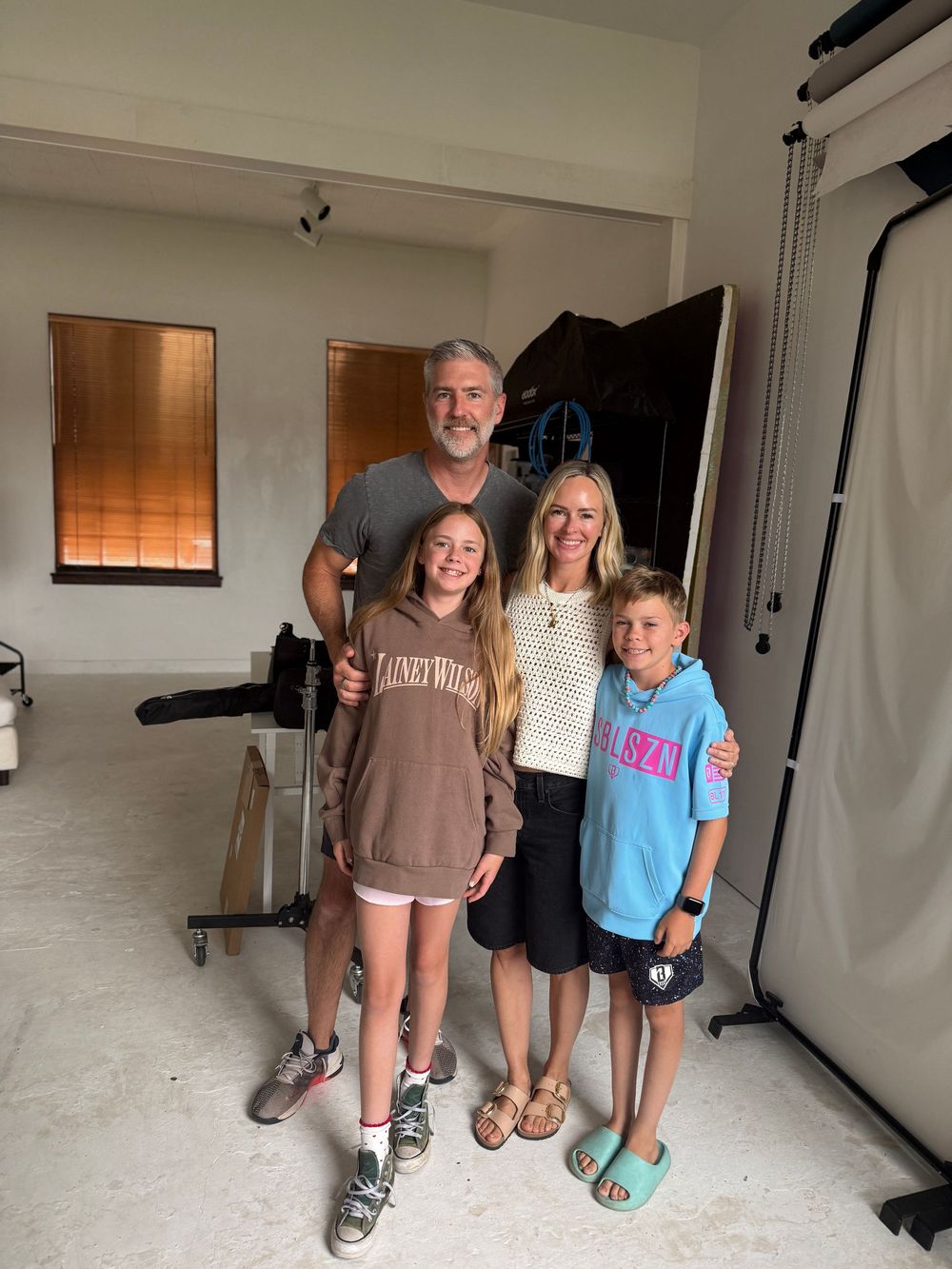Family of four posing together indoors in a photography studio, smiling for a casual portrait photo.