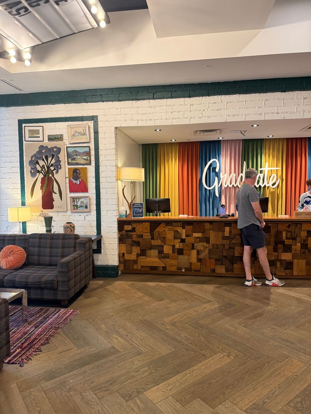 Graduate Hotel lobby with colorful rainbow striped reception desk, herringbone wood floors, and eclectic lounge seating area.