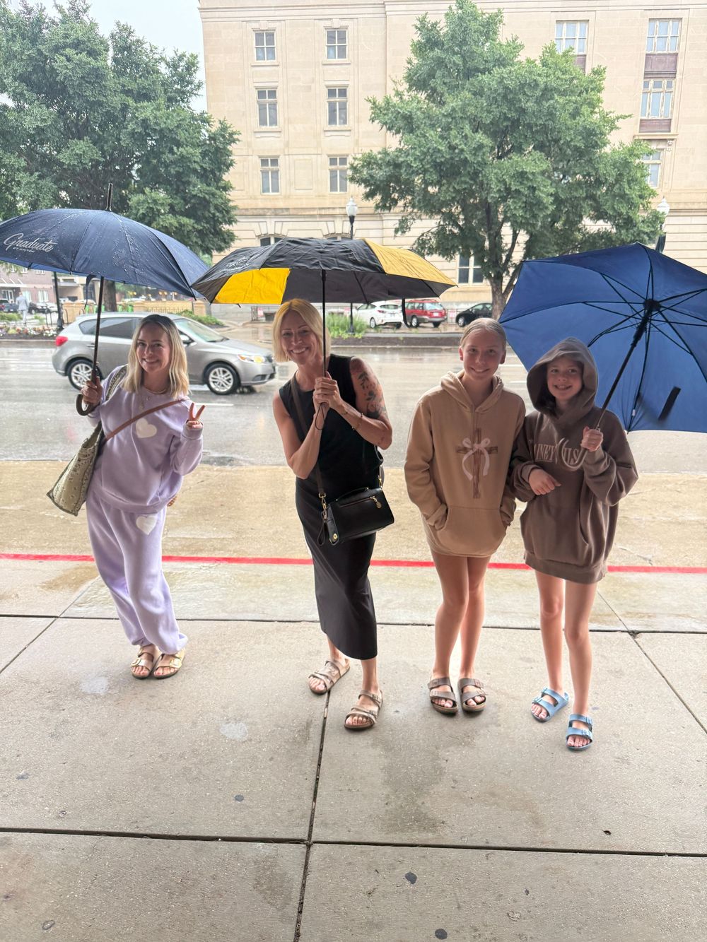 Four women standing under colorful umbrellas on a rainy day outside a building.