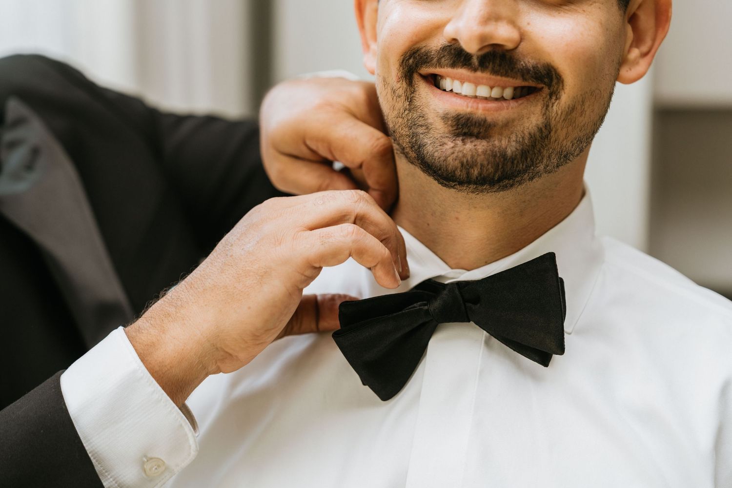 Close-up of the groom adjusting his black bow tie before the wedding ceremony.