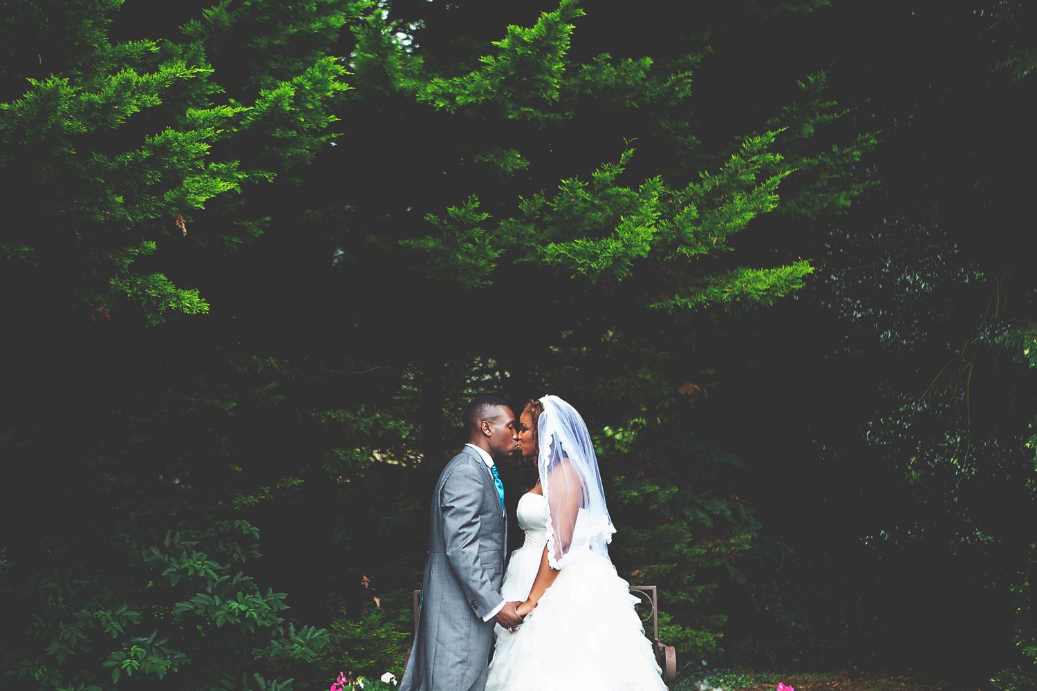 Bride and groom sharing a romantic kiss outdoors, surrounded by lush green trees on their wedding day.