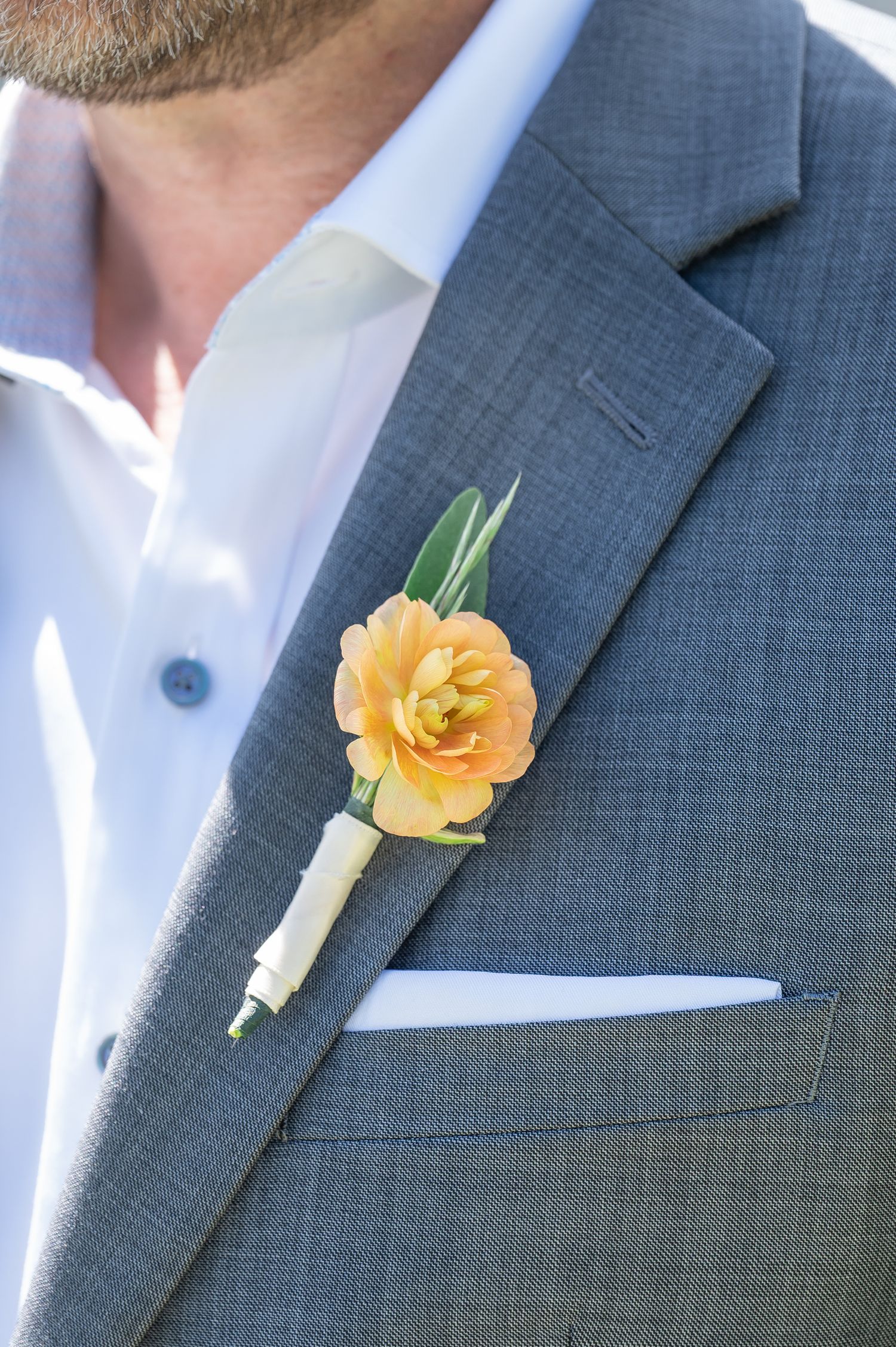 Gray suit lapel with peach ranunculus boutonniere and white pocket square, perfect for a wedding for Vail elopement