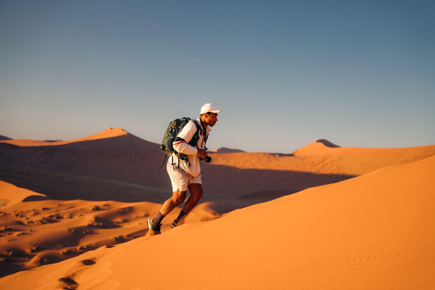 homme qui escalade la dune 45 dans le désert du namib avec son sac à dos et sa casquette blanche
