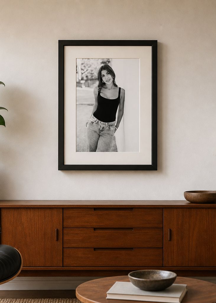 Black and white framed photo of a young woman in jeans and tank top displayed above a mid-century modern wooden sideboard.