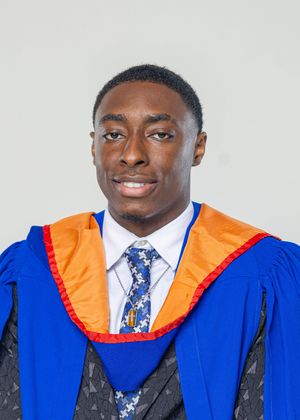 Young man in blue and orange graduation gown and patterned tie posing for official graduation portrait photo.