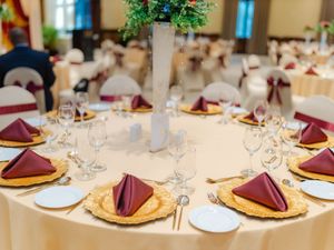 Elegant banquet table set with gold charger plates, burgundy napkins, crystal glassware, and floral centerpiece for a formal event.