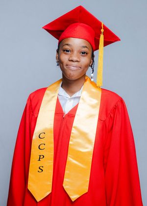 A smiling graduate wearing a red cap and gown with a gold CCPS honor stole poses for a portrait photo.