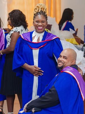 Two graduates in blue academic robes smile at a university graduation ceremony.
