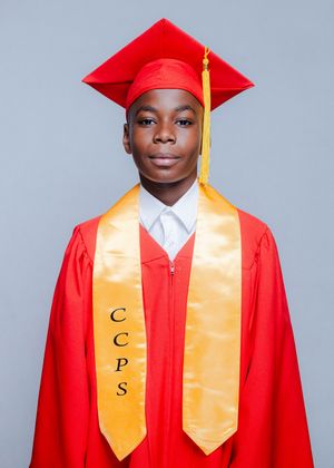 Young graduate in red cap and gown with gold CCPS stole poses for formal portrait photo.