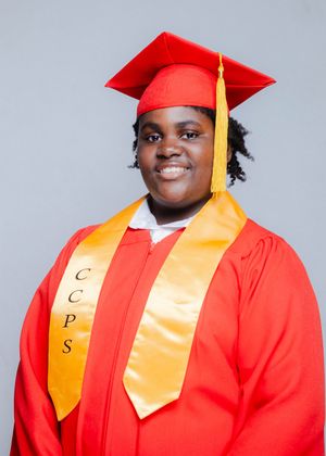 Smiling graduate wearing red cap and gown with gold CCPS honor stole for graduation portrait.