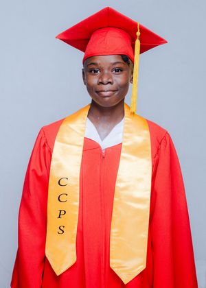 Graduate in red cap and gown with gold CCPS stole posing for official graduation portrait photo.