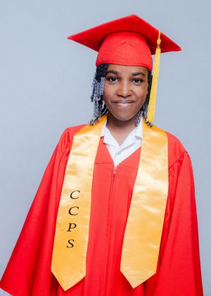 Graduate smiling in red cap and gown with gold CCPS honor stole against gray background.