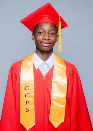 Young graduate in red cap and gown wearing gold CCPS stole smiles for graduation photo.