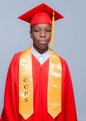 Graduate in red cap and gown with gold CCPS honor stole poses for formal school portrait.