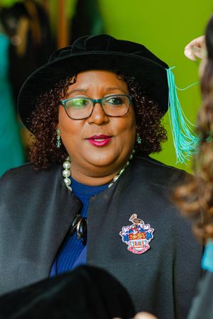 Woman wearing doctoral cap and academic gown with university crest brooch at graduation.