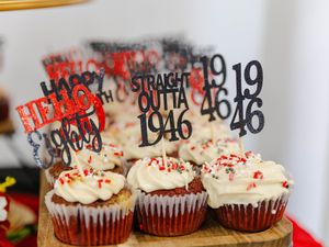 Cupcakes with white frosting and toppers reading Straight Outta 1946 and Happy 40th on a wooden stand.