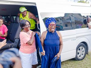 A joyful woman in blue dress laughs while being greeted outside a white van at an outdoor gathering.