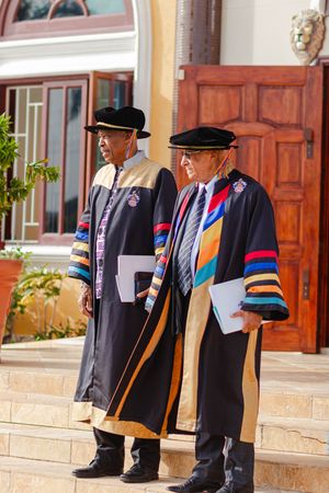 Two senior academics in colorful doctoral robes and mortarboard hats at graduation ceremony.