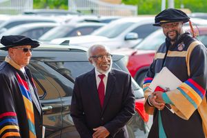 Three men in academic regalia and formal attire conversing outdoors at a graduation event.