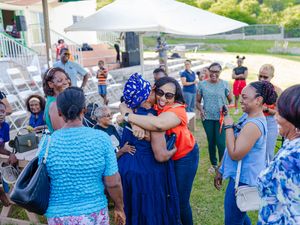 People sharing warm hugs and greetings at an outdoor social gathering with guests in colorful attire.