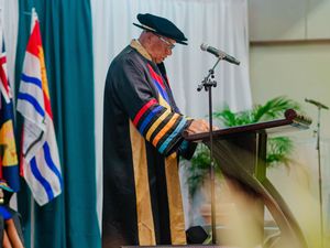 University chancellor in ornate academic regalia delivering speech at podium during graduation.