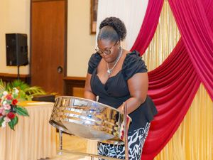 Woman playing a steel pan drum at an elegant event with red and gold drape backdrop.