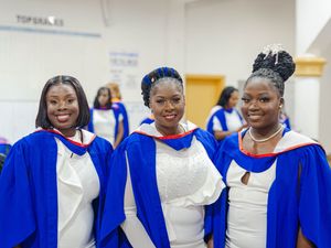 Three smiling female graduates in blue and white robes at a graduation ceremony.