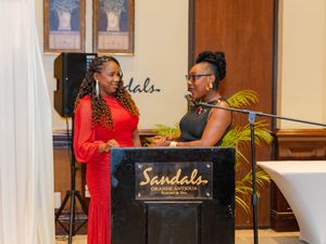 Two women speaking at a Sandals Grande Antigua Resort podium during a formal event.