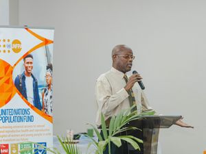 A man speaks at a UNFPA United Nations Population Fund event, holding a microphone at a podium.