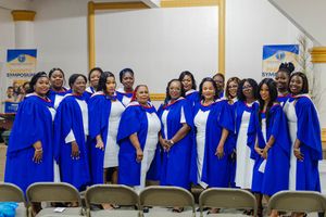 Group of graduates in blue and white robes pose together at graduation ceremony.