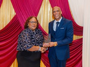 Two professionals share an award at a formal ceremony, posing together in front of a red and gold draped backdrop.