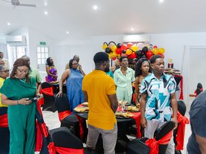 Guests mingle at a festive indoor party with red and black decor, colorful balloons, and a food table.