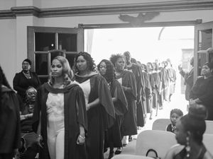 Black and white photo of graduates in academic gowns processing into a graduation ceremony hall.
