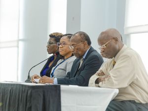 Four professionals seated at a panel discussion table with microphones in a modern conference room.