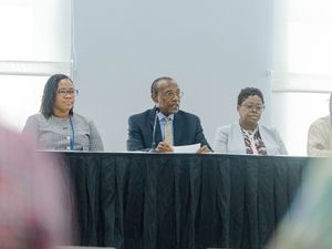 Three professionals seated at a panel discussion table with black skirting at a formal conference event.