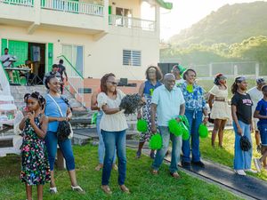 Group of people standing outdoors on grass near a building, holding green items at a community gathering event.