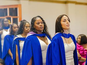 Female graduates in blue robes stand during academic procession at ceremony.