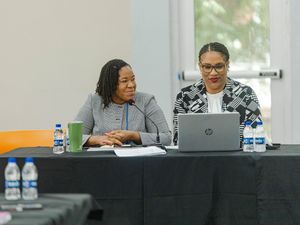 Two professional women collaborating on HP laptop at conference table during meeting.