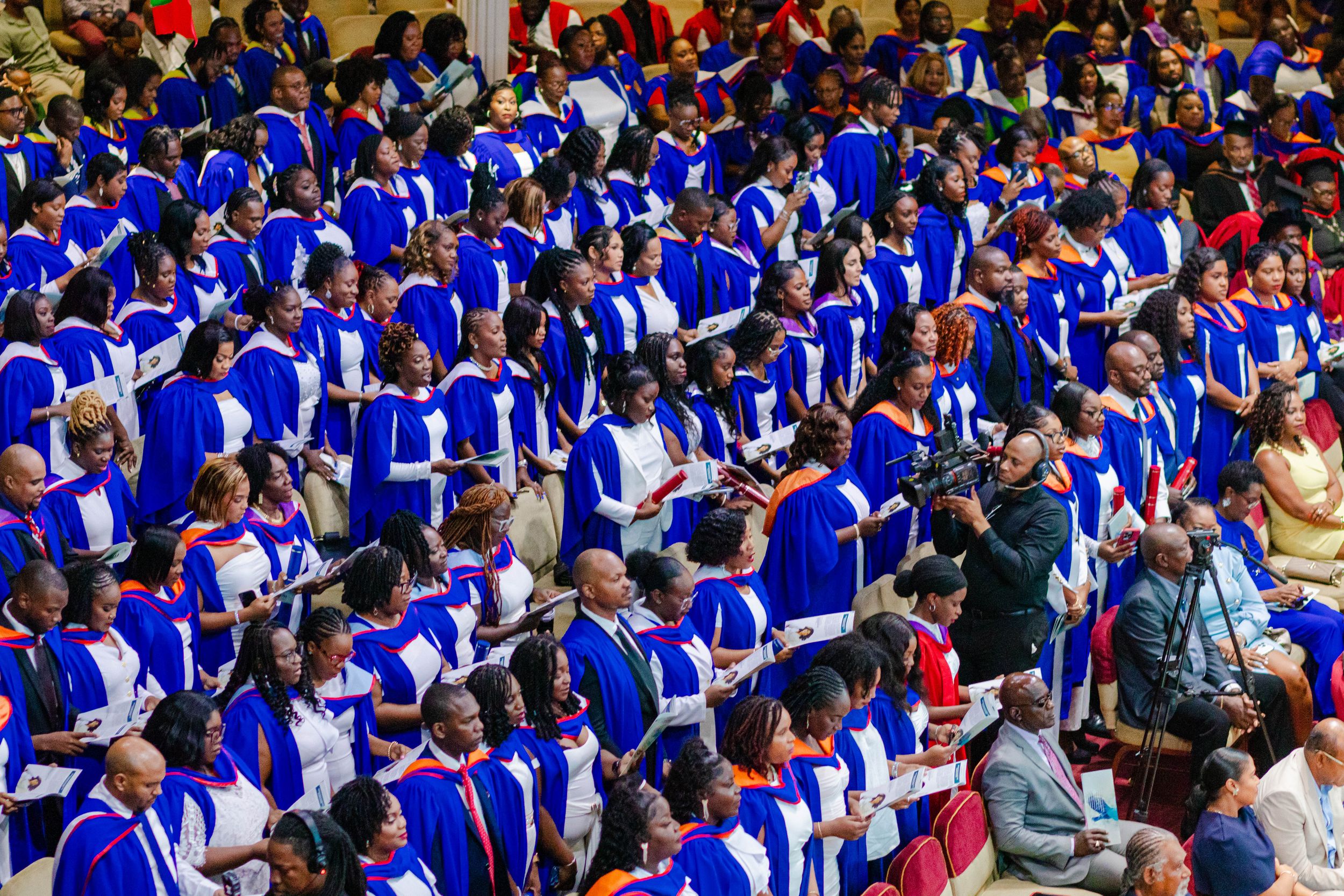 Large group of graduates in blue robes seated at a university graduation ceremony.