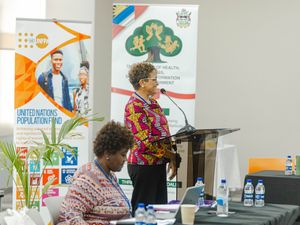 Woman in colorful blouse presenting at podium beside United Nations Population Fund banner.