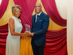 Two professionals pose with a crystal award at a formal ceremony with red and gold drape backdrop.