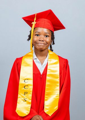 Young graduate smiling in red cap and gown with gold CCPS stole for graduation portrait.