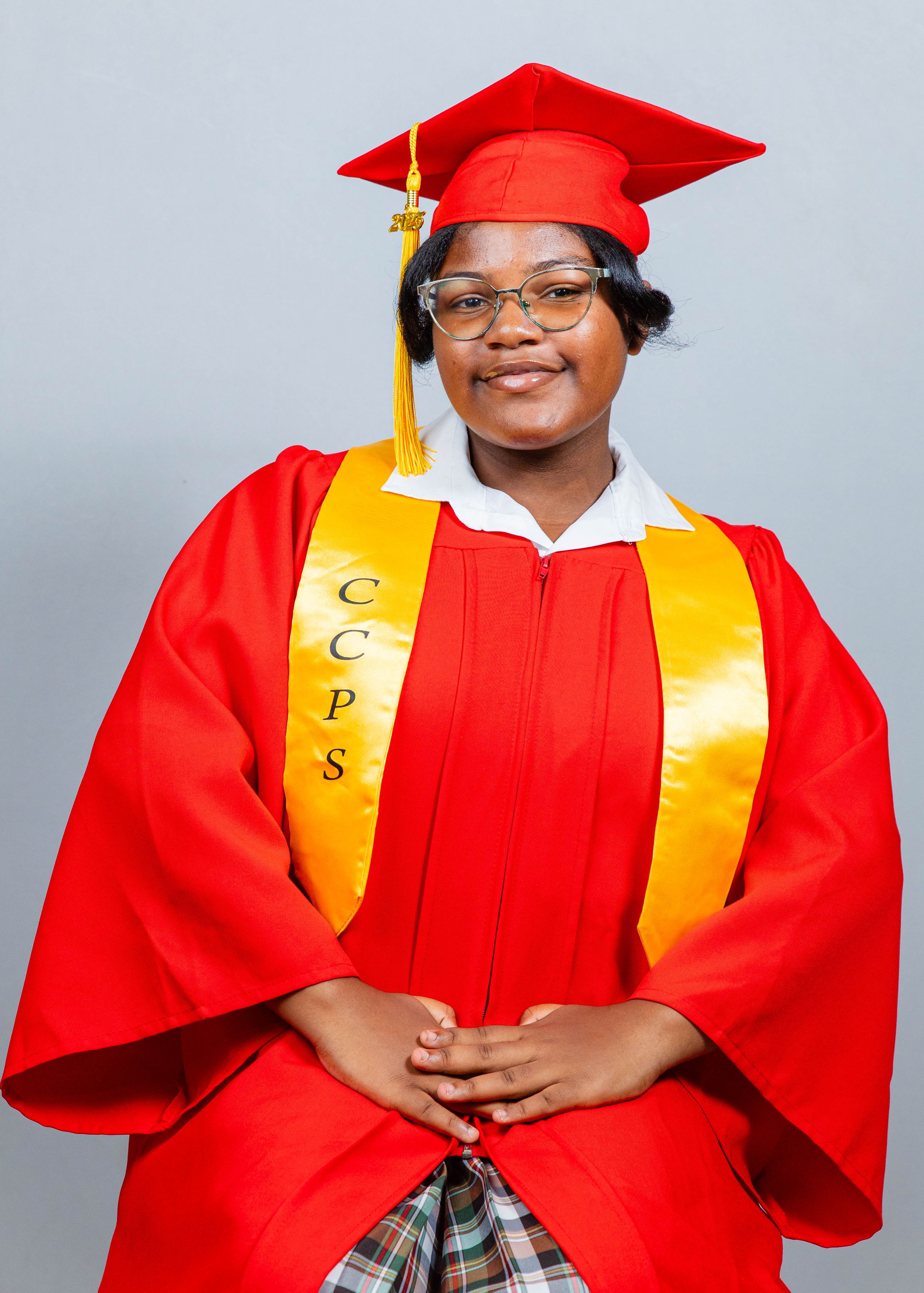 A smiling graduate in red cap and gown with gold CCPS stole poses for a professional graduation portrait.