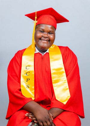 Smiling graduate in red cap and gown with gold CCPS honor stole seated for graduation photo.