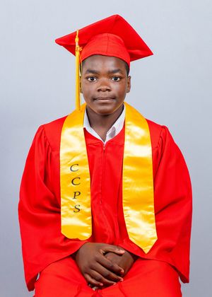 Young graduate in red cap and gown with gold CCPS honor stole sits for formal graduation photo.