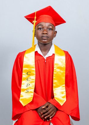Young student in red graduation cap and gown with gold CCPS stole stands for formal portrait.