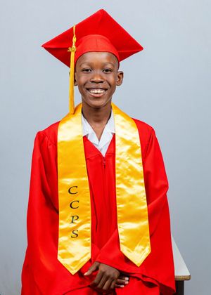 Smiling graduate in red cap and gown with gold CCPS stole during official graduation portrait session.