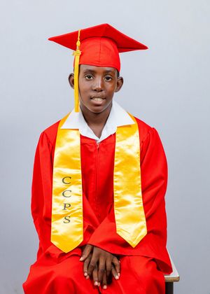 Young graduate in red cap and gown with gold CCPS stole, seated for formal graduation portrait photo.