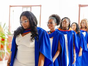 Female graduates in blue academic robes walking in procession at a graduation ceremony.